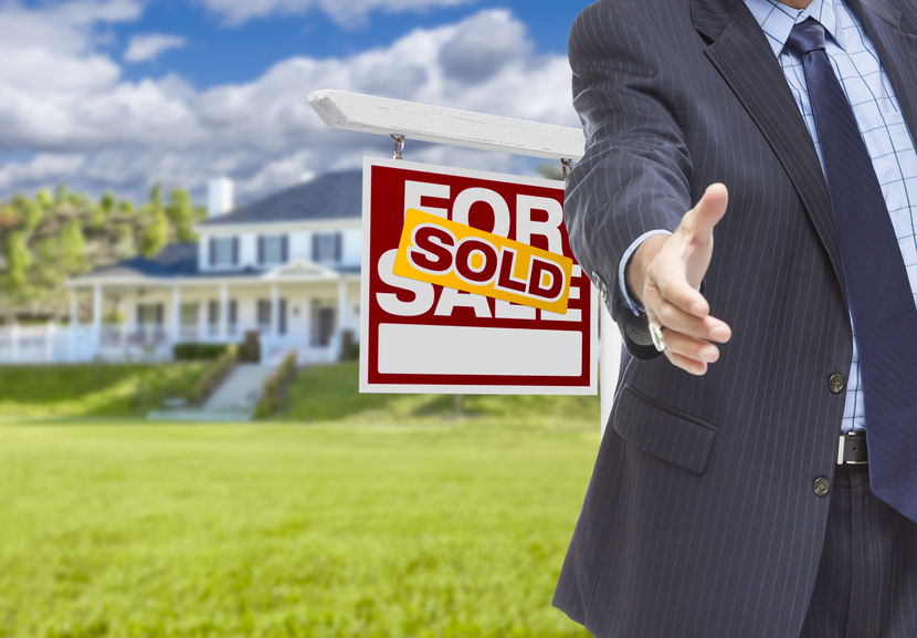 Real Estate Agent Reaches for Handshake with Sold Sign and New House Behind.